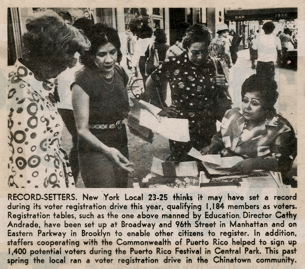 Kathy Andrade seated at a voter registration table on a busy New York street, assisting women with forms during a 1976 union-led voter registration drive.