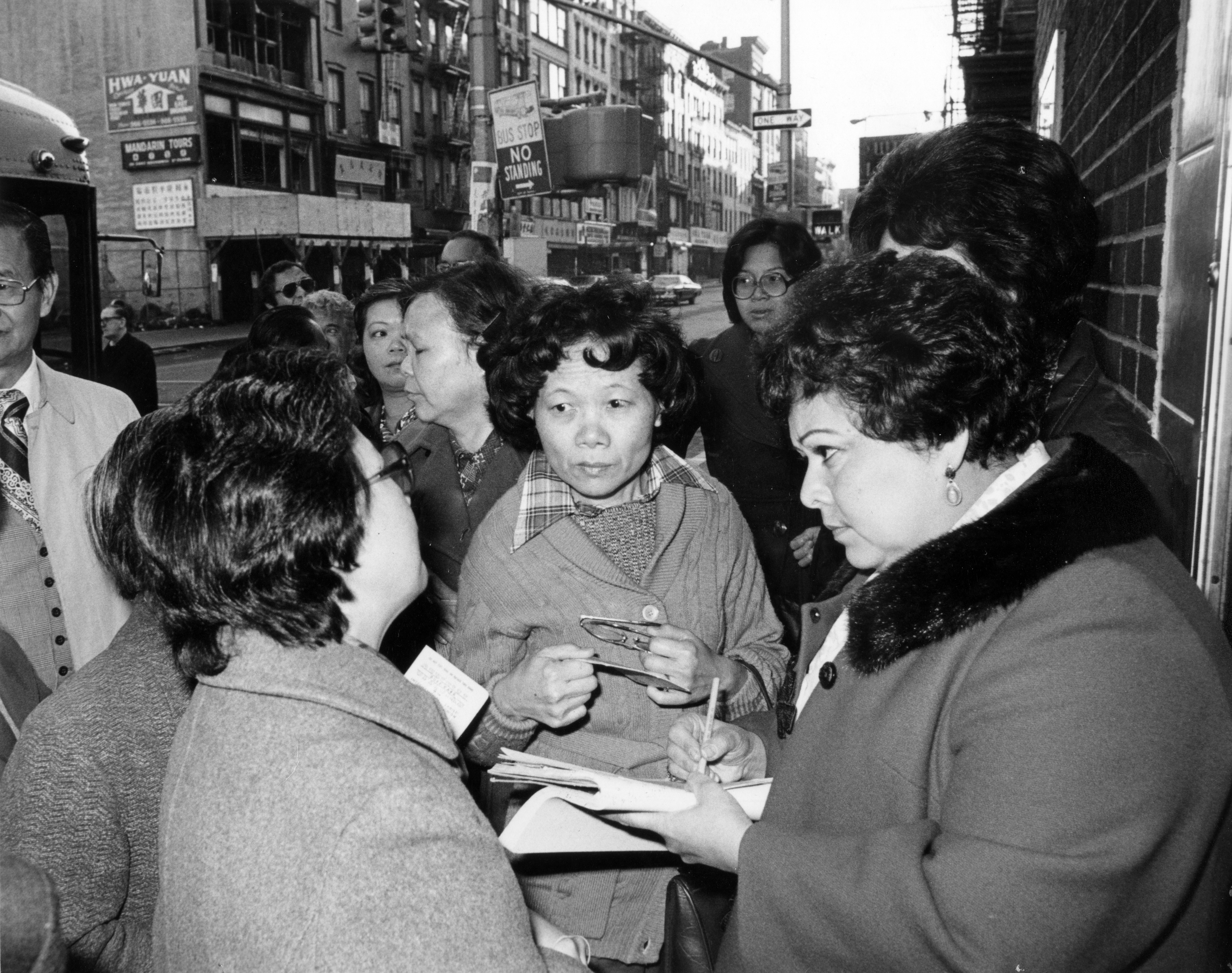 Kathy Andrade with union members in Chinatown, holding a pen and clipboard while checking names before workers board a van to the union health center, 1978.