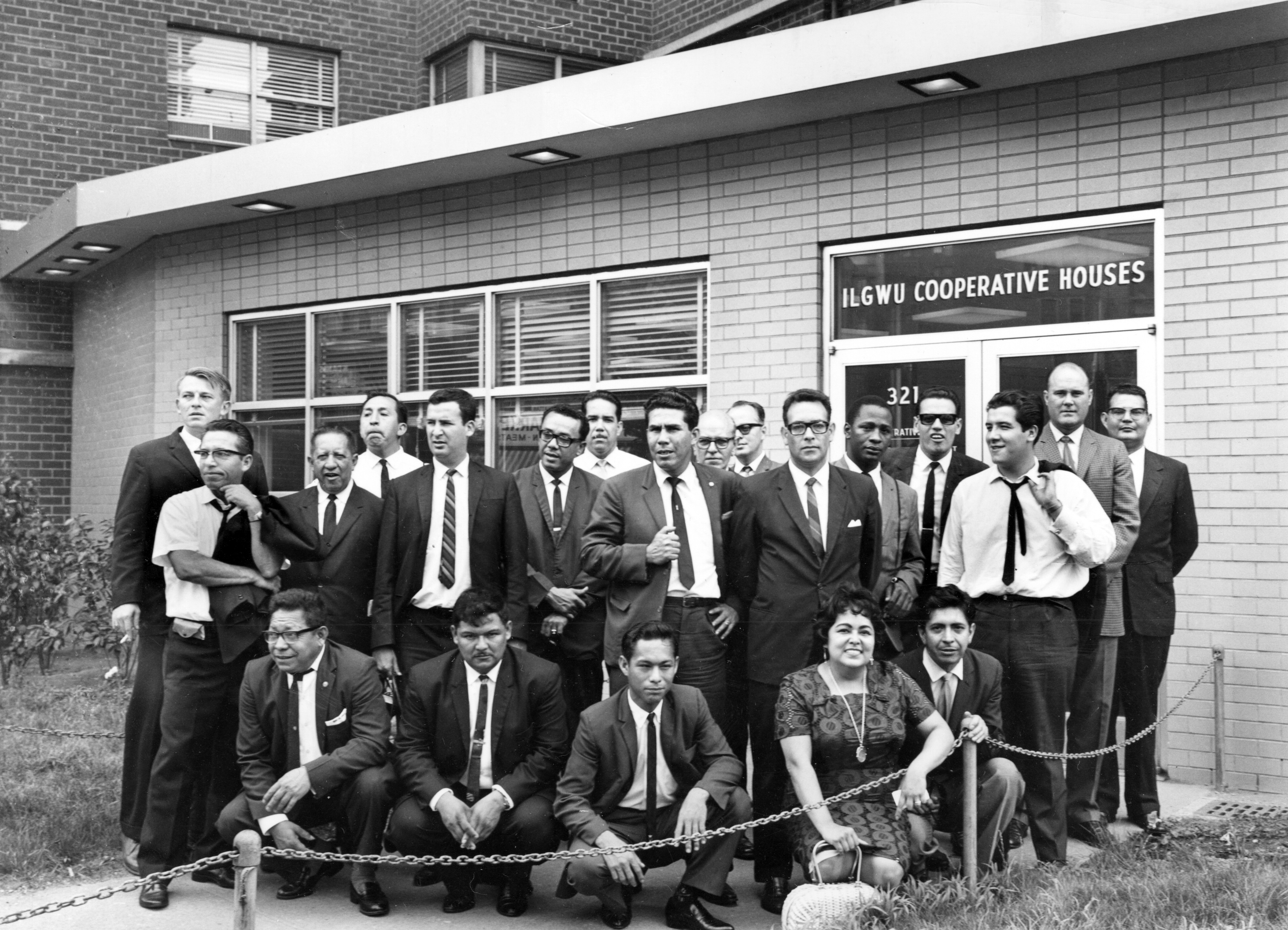 Kathy Andrade seated with a delegation of men in suits outside the ILGWU Cooperative Houses, posing for a group photograph.
